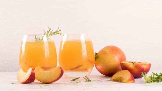 Homemade peach juice with ice cubes and rosemary leaves in glass on marble stone background.