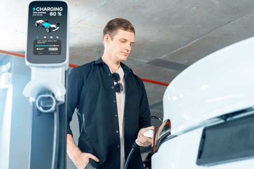 Young man travel with EV electric car to shopping center parking lot charging in downtown city showing urban sustainability lifestyle by green clean rechargeable energy of electric vehicle innards