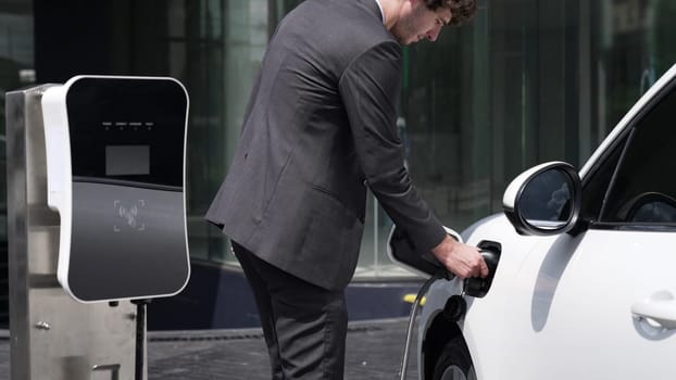 Progressive businessman unplugs charger plug from charging station to his electric car before driving around city center. Eco friendly rechargeable car powered by sustainable and clean energy.