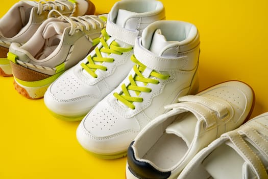 Several pairs of fashion trendy sport shoes on yellow background close up