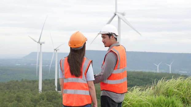 Male and female engineers working on a wind farm atop a hill or mountain in the rural. Progressive ideal for the future production of renewable, sustainable energy.