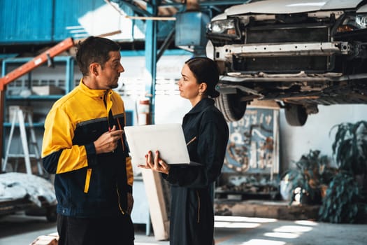 Two vehicle mechanic working together, conduct car inspection with laptop. Automotive service technician in uniform carefully make diagnostic troubleshooting to identify error. oxus