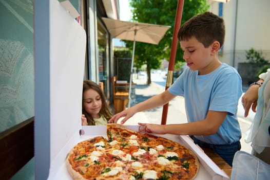 Adorable children, a teenage boy and little kid girl snacking outdoors, eating a delicious freshly baked Italian Margherita pizza with a crispy crust in the street. Italian lifestyle, cuisine, culture