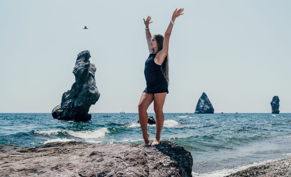 Woman travel sea. Young Happy woman in a long red dress posing on a beach near the sea on background of volcanic rocks, like in Iceland, sharing travel adventure journey