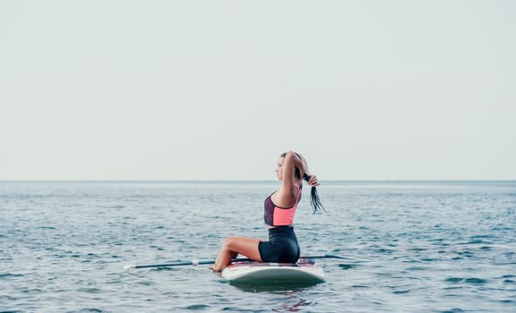 Silhouette of woman standing, surfing on SUP board, confident paddling through water surface. Idyllic sunset or sunrise. Sports active lifestyle at sea or river.