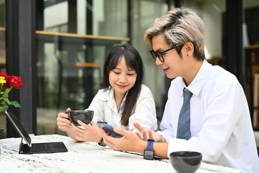 Smiling female and male coworkers talking during coffee break near office building.