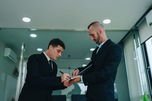 Two business men meeting to talking or discuss marketing work in workplace using paperwork, calculator, computer to work