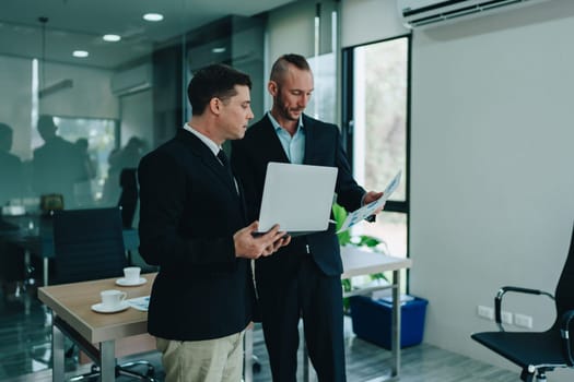 Two business men meeting to talking or discuss marketing work in workplace using paperwork, calculator, computer to work