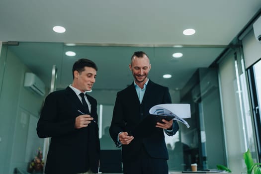 Two business men meeting to talking or discuss marketing work in workplace using paperwork, calculator, computer to work