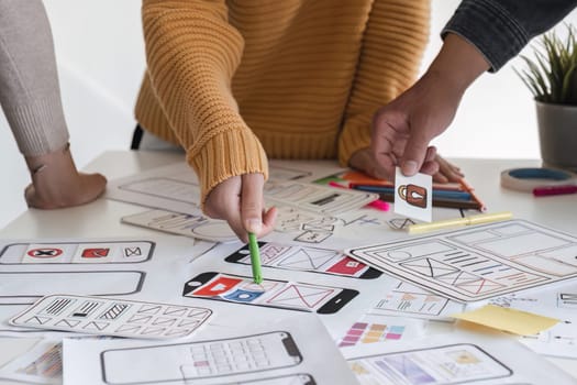 Image of a team of developers brainstorming UI and UX design ideas for a mobile app on a paper wireframe interface. Planning the user interface development team for an intuitive UI design..