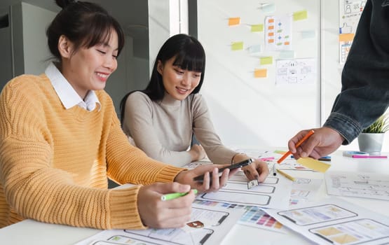 Image of a team of developers brainstorming UI and UX design ideas for a mobile app on a paper wireframe interface. Planning the user interface development team for an intuitive UI design..