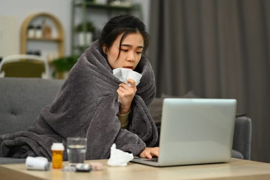 Young woman wrapped in blanket having online medical consultation on laptop. Healthcare and technology concept.