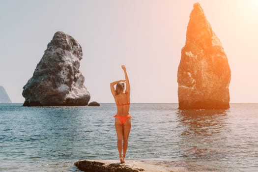 Woman travel sea. Young Happy woman in a long red dress posing on a beach near the sea on background of volcanic rocks, like in Iceland, sharing travel adventure journey