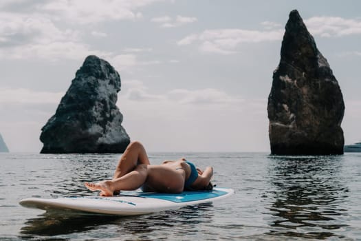 Close up shot of beautiful young caucasian woman with black hair and freckles looking at camera and smiling. Cute woman portrait in a pink bikini posing on a volcanic rock high above the sea