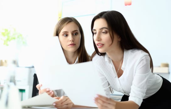Portrait of smart businesswoman looking at important document with significant information about company profit and standing near concerned colleague. Accounting office concept