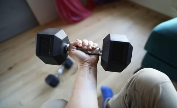 Close-up of man lifting heavy dumbbell for strong fit arm. Fitness metal equipment for train indoors. Stay athletic on quarantine period. Sport and active lifestyle concept