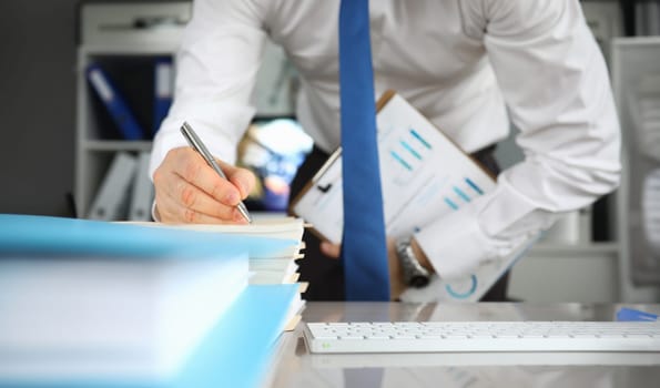 Close-up of employee finish annual report for conference meeting. Businessman holding clipboard with diagrams. Man in trendy costume in company office. Business concept