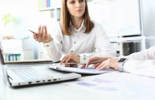 Focus on smart businesswoman sitting indoors and holding metallic writing pen. Witty female manager discussing something important with colleague. Accounting office concept. Blurred background