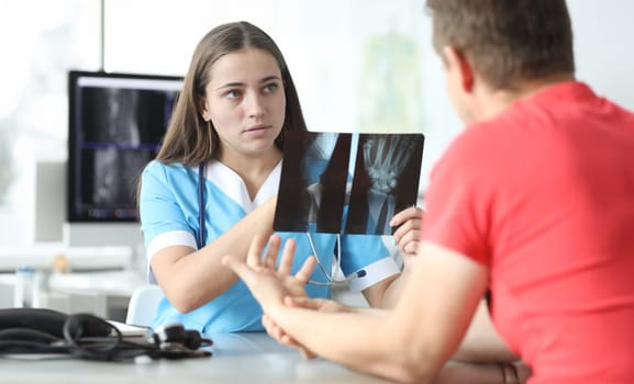 Portrait of focused radiologist discussing x-ray of hand with injured patient. Professional surgeon making treatment appointments. Medicine and healthcare concept