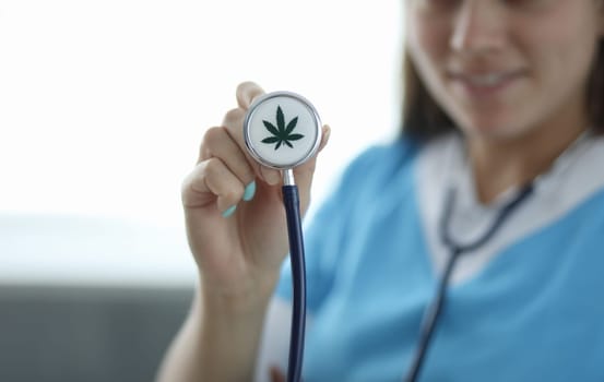 Close-up of female hand holding stethoscope with sign of cannabis. Doctor using medical equipments. Pain medication. Healthcare and medical marihuana concept