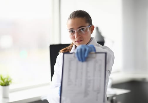 Portrait of lab assistant holding clipboard with results of tests. Smiling scientist showing documents. Laboratory interior on background. Chemical experiments concept