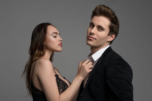 Sexy young girl in black lace lingerie and a handsome man in black suit and shirt portrait on gay background