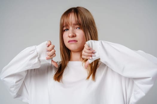 Young teen girl expressing disapproval while wearing a white oversized sweater against a plain backdrop close up
