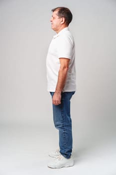 Mature man standing sideways in casual attire against a plain background