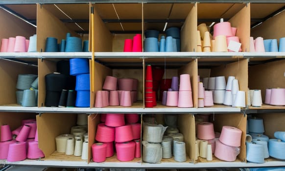 Spools with different color thread on shelves at knitting factory shot