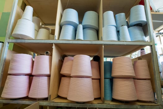 Spools with different pastel color thread on shelves at knitting factory shot