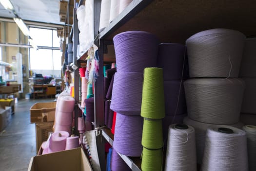 Spools with different color thread kept on shelves at knitting factory shot