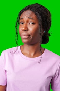 Young woman with curly hair shows a skeptical expression against a bright green background in studio