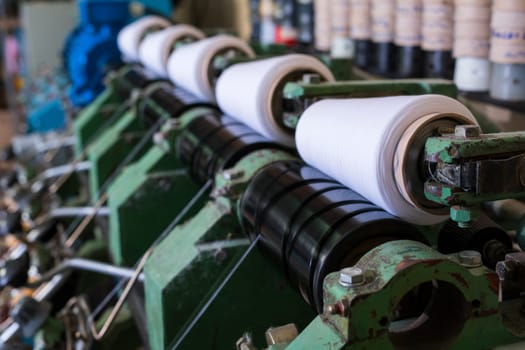 Big spools with white thread at rewinding machine at knitting shop view