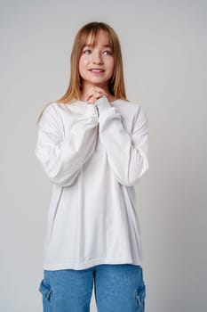 Young woman in a white long-sleeve shirt thoughtfully poses with a hand on her chin in a minimalistic indoor setting