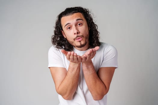 A man with curly hair blows a kiss to the camera while wearing a white t-shirt close up