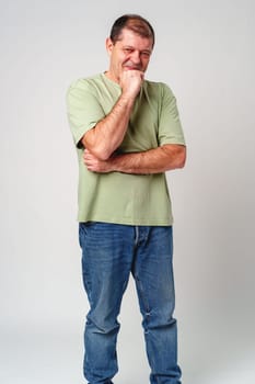 A man in a light green shirt and jeans stands against a plain background with a thoughtful expression close up