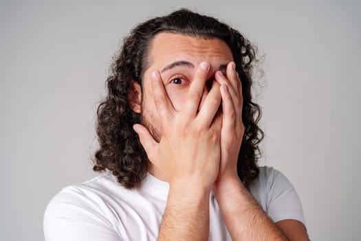 Young man covers his face with hands in a moment of surprise or shock against a neutral background close up
