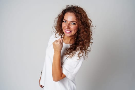 Cheerful woman with curly hair smiling confidently and gesturing with her fist in a bright studio setting