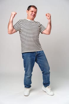 A cheerful man in a striped shirt strikes a playful pose against a light background, showcasing joy and confidence close up