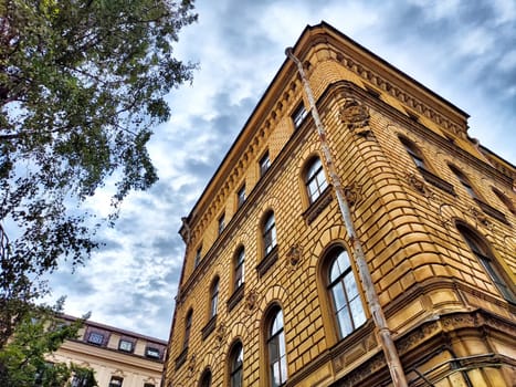 A yellow brick building with arched windows stands tall against cloudy sky