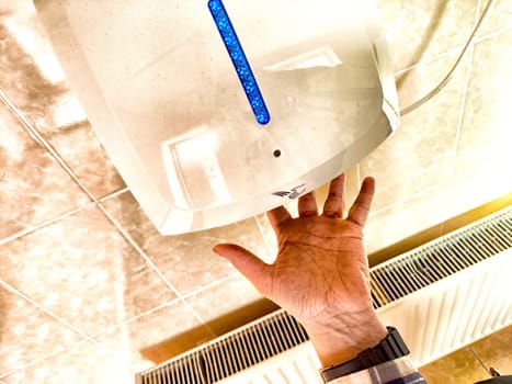 A person places their hand under a hand dryer in restroom, utilizing modern technology for quick drying