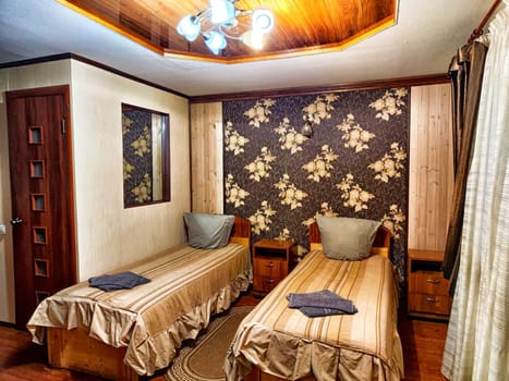This welcoming twin bedroom features floral wallpaper and wooden accents, offering a cozy atmosphere with ample natural light and comfortable bedding.