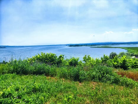 A peaceful lake is framed by vibrant green vegetation under clear blue skies.