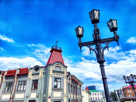 A charming historic structure displays unique architectural details beneath a bright blue sky filled with clouds, set in a lively urban environment.