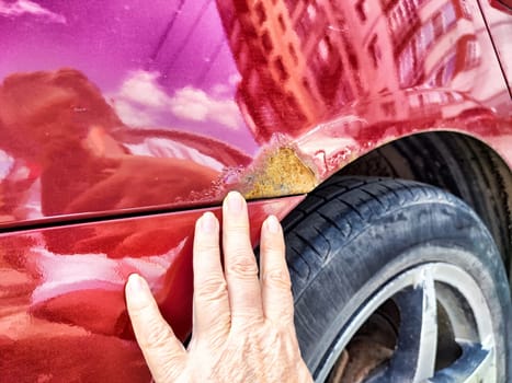 A person is pointing directly at a rusty, weathered place on a car that shows signs of age and decay, highlighting its condition