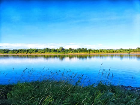 A tranquil river reflects the azure sky, surrounded by vibrant green foliage under the warm afternoon sun.