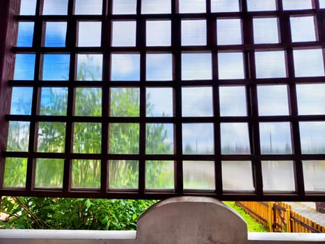 A detailed view of a wooden lattice window reveals lush greenery and a sunny blue sky outside on a peaceful day.