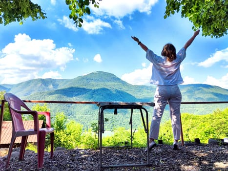 A woman raises her arms in joy while overlooking breathtaking mountain landscape filled with lush greenery