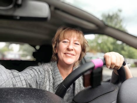 A middle aged woman is happily smiling as she drives her car, enjoying the sunny day outside.