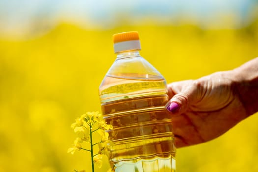 A hand gently grasping a bottle filled with golden oil, set against a backdrop of vibrant yellow flowers